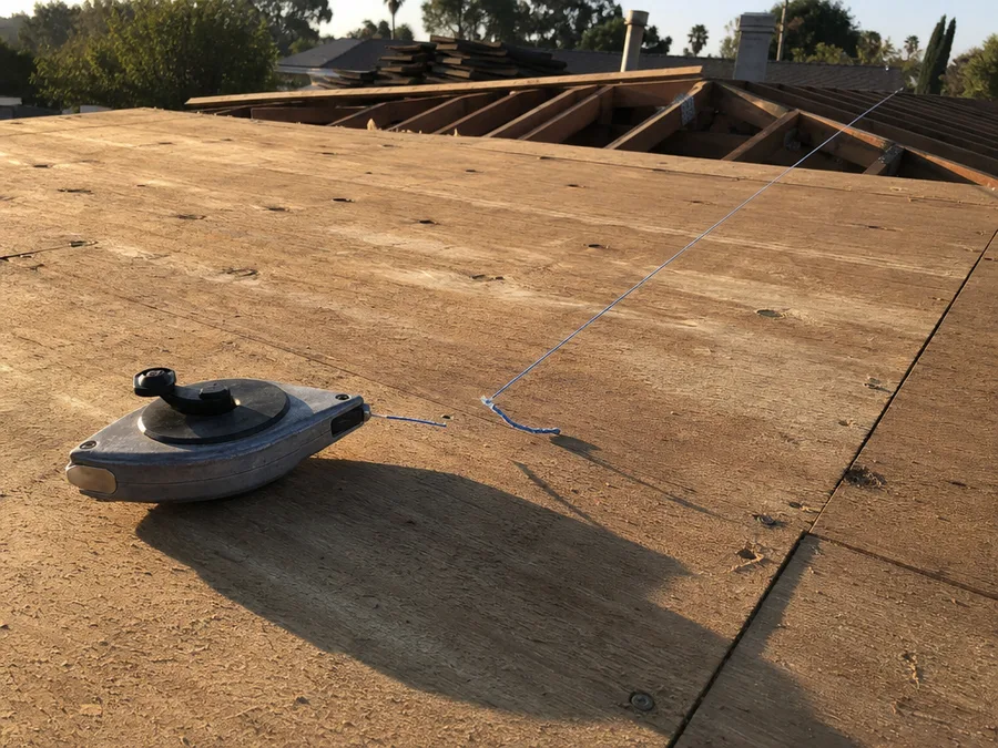 A chalk line reel on bare plywood roof deck with a snapped blue line running across it