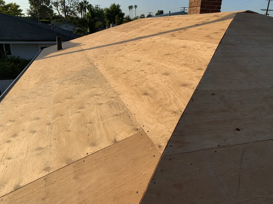 A roof deck sheeted in fresh plywood with straight rows of nail heads across the slope, ready for a sheathing inspection