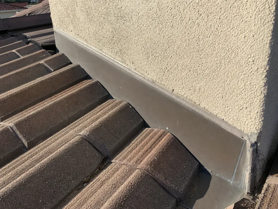 Sheet metal counterflashing lapped into a stucco chimney chase where it meets a tile roof